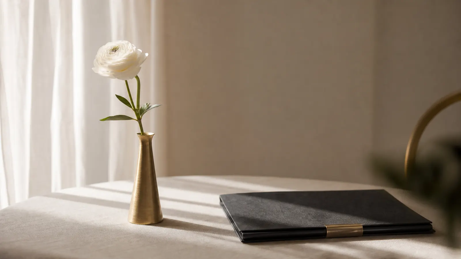 A white flower in a brass vase beside a closed folder